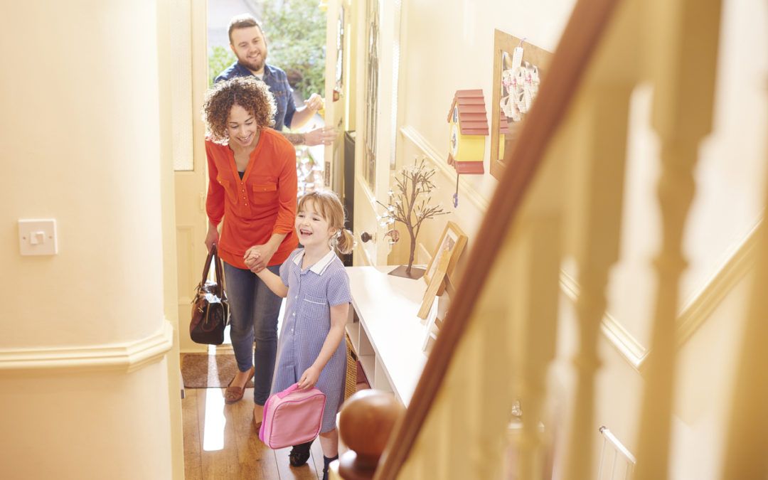 A family of three walking into a house, with parents leading the way for a child