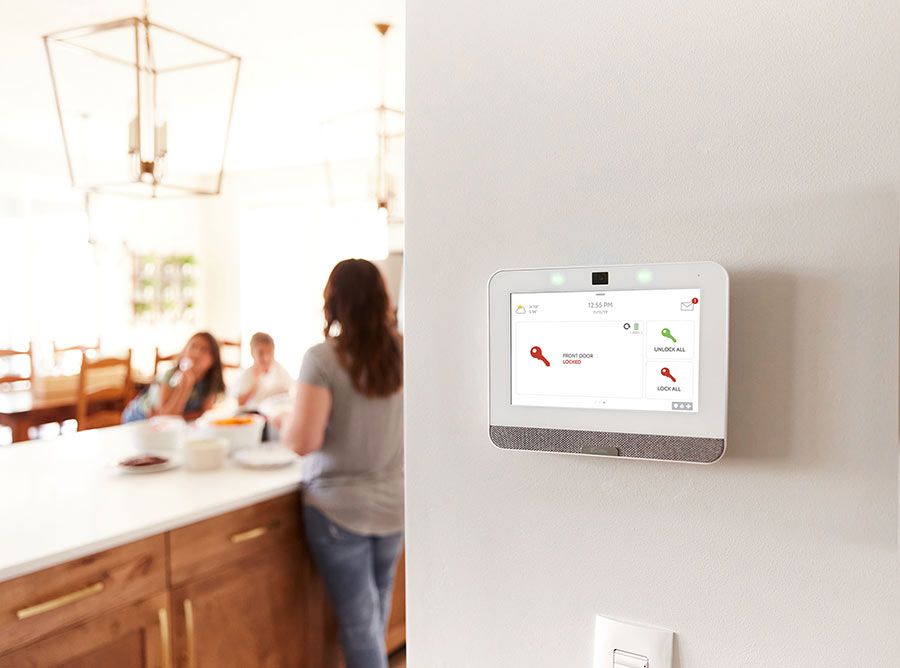 A smart home device mounted on a wall, with a family seen in the background