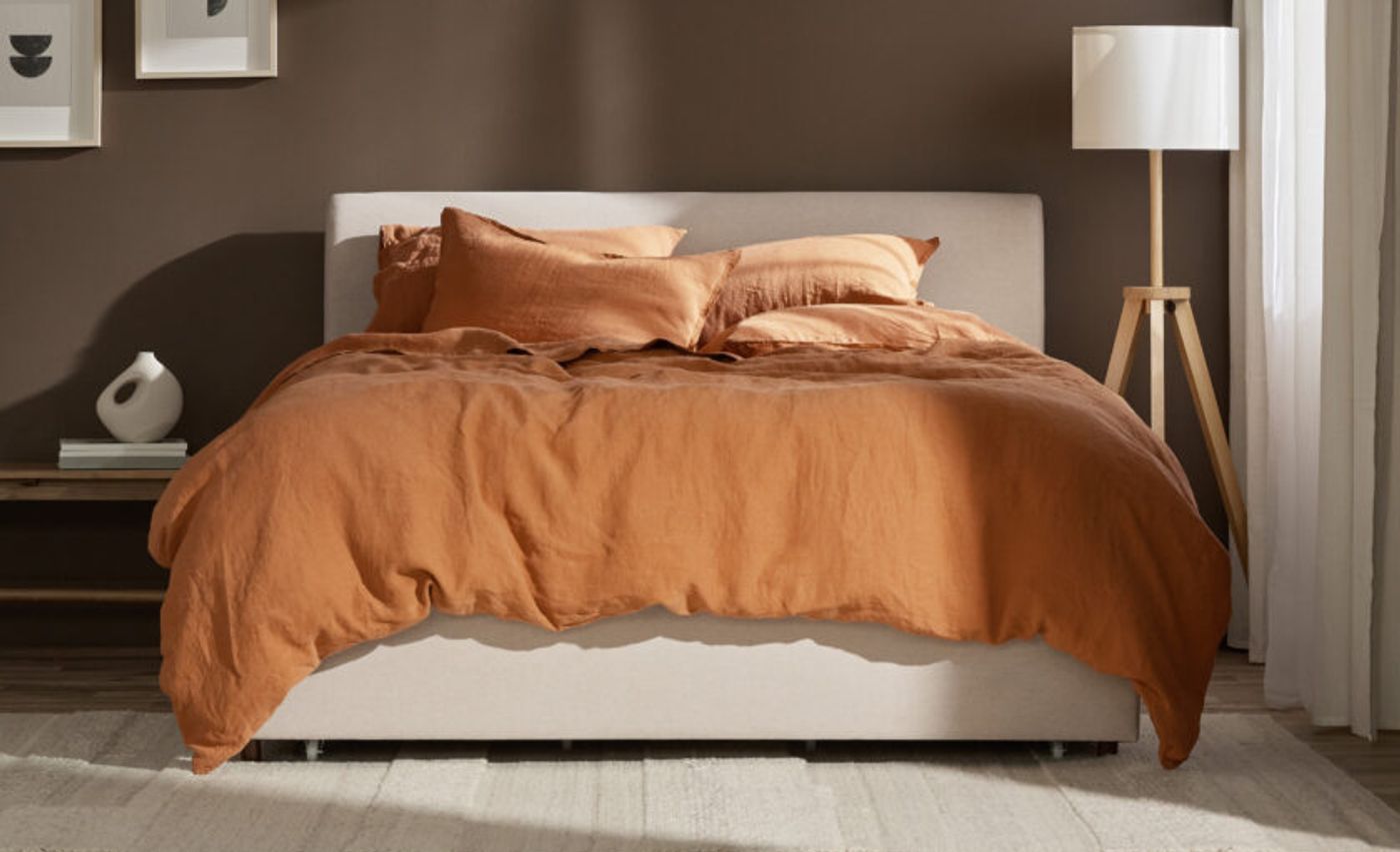 Bed made with rust orange Silk & Snow flax linen bedding in a warm bedroom