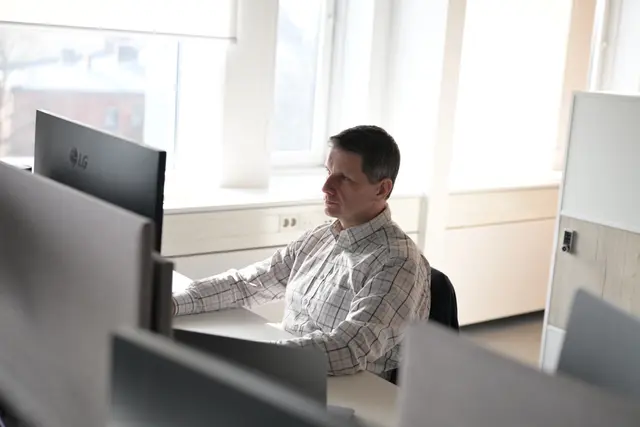 Man sitting in chair by desktop and works in front of a laptop.
