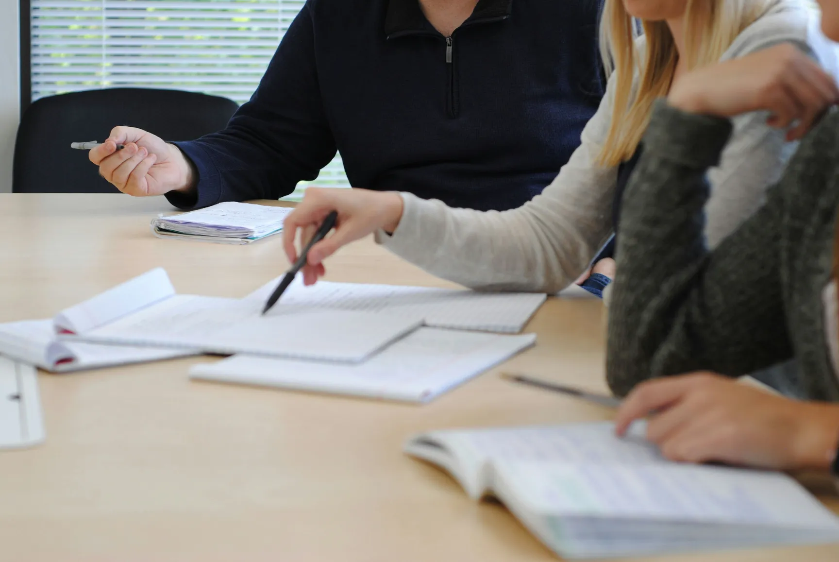 Claude responded: Three people reviewing documents and notebooks at a meeting table in a bright office environment.Three people reviewing documents and notebooks at a meeting table in a bright office environment.