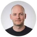 Smiling man in a black shirt photographed against a background in a circular crop portrait photo.