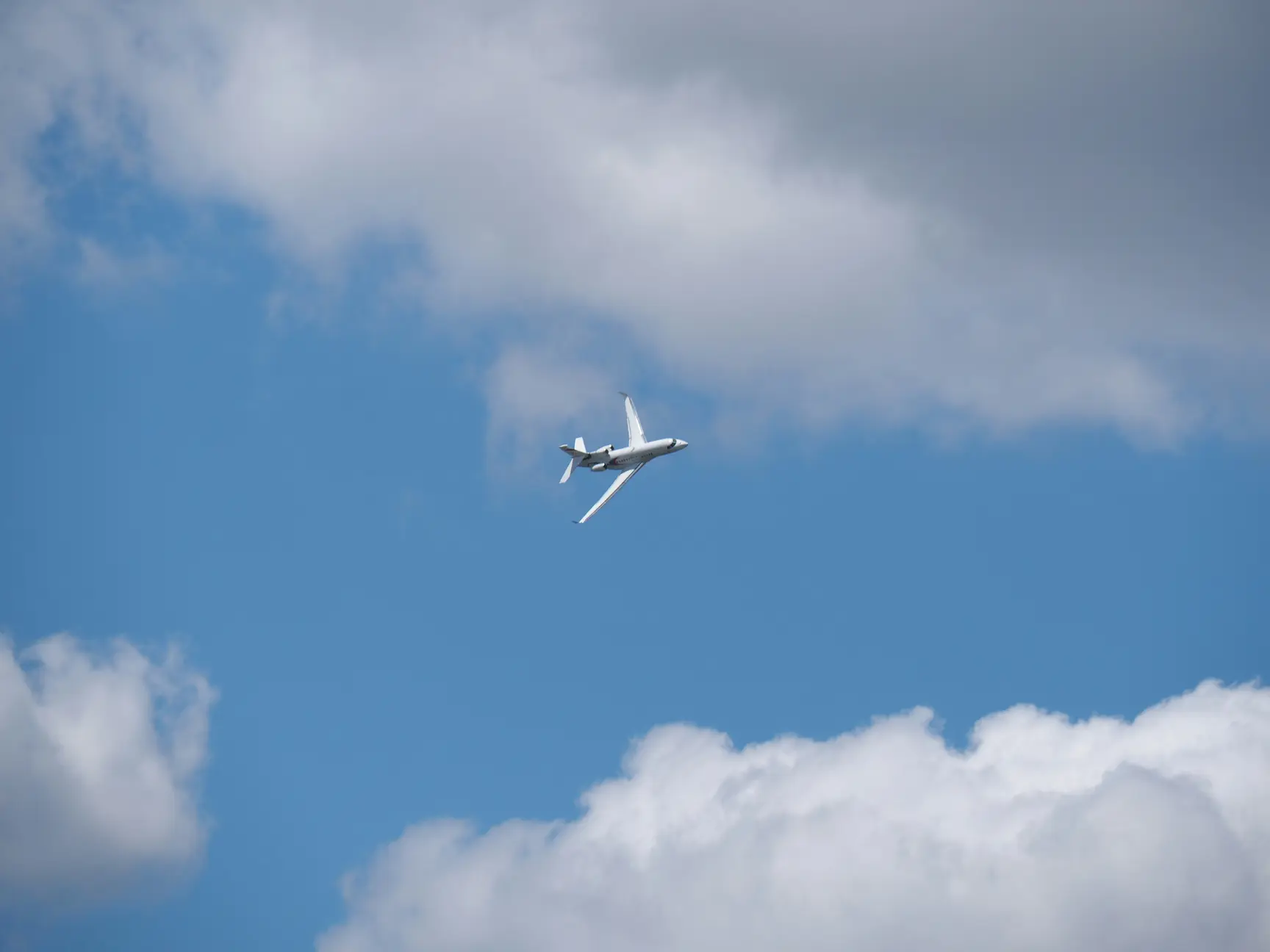 A white commercial aircraft flying at altitude against a blue sky with scattered white and grey clouds.A white commercial aircraft flying at altitude against a blue sky with scattered white and grey clouds.