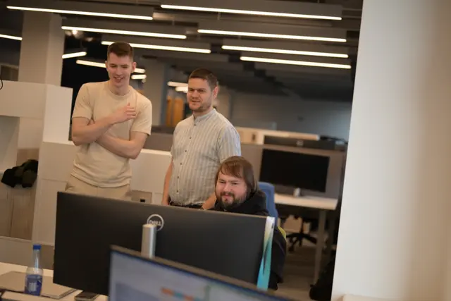 Three man standing in an office looking at a computer.