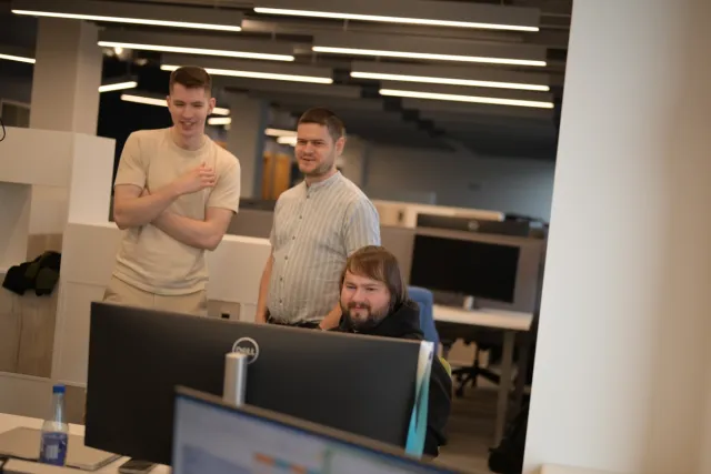 Three man standing in an office looking at a computer.