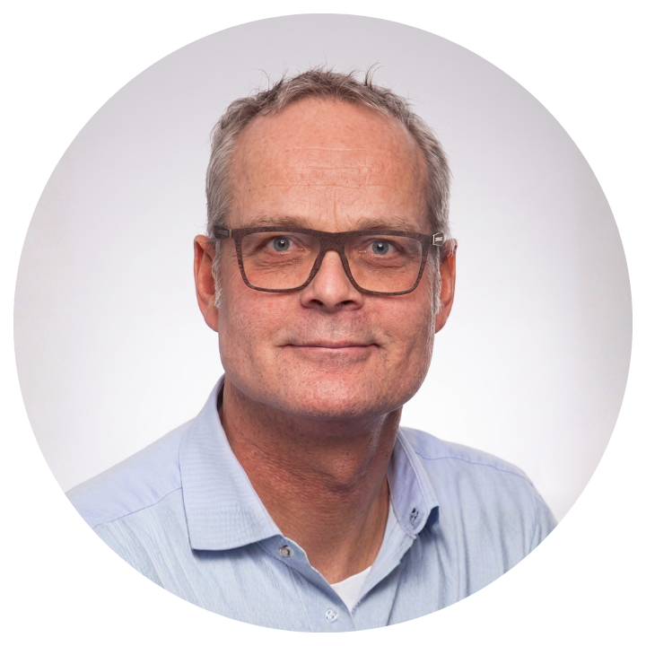 Man with glasses wears a blue shirt and is photographed against a white background.