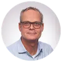 Man with glasses wears a blue shirt and is photographed against a white background.