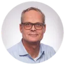 Man with glasses wears a blue shirt and is photographed against a white background.