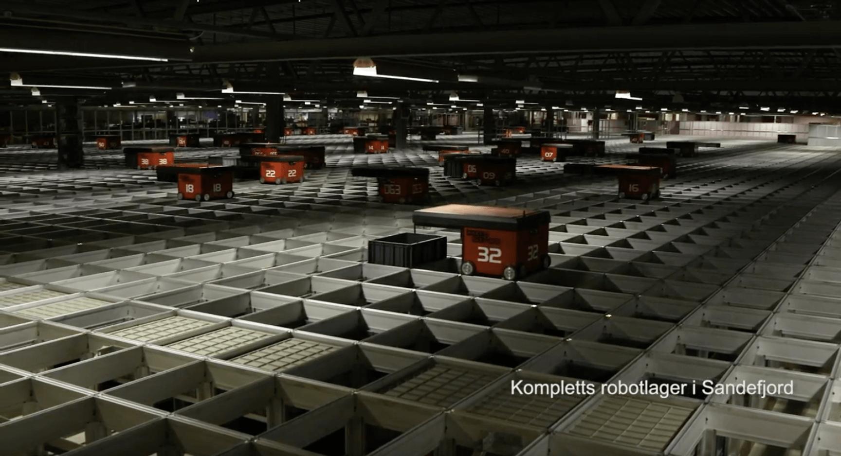 Large automated warehouse with numbered orange robots moving across a grid floor, from Komplett's facility in Sandefjord.