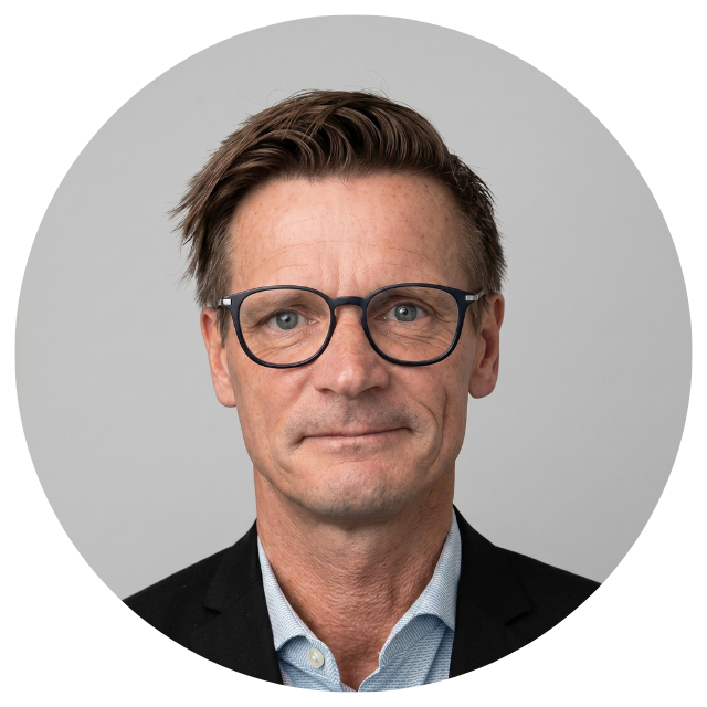 Smiling man in glasses photographed against white wall