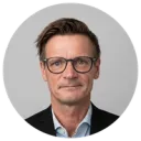 Smiling man in glasses photographed against white wall