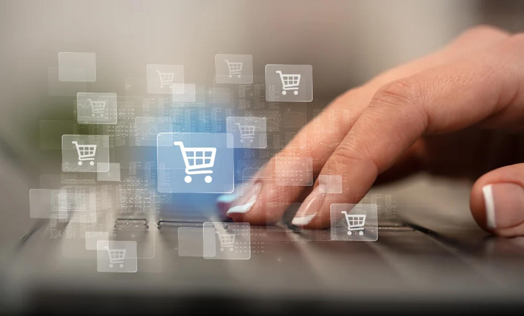 Hand pressing a laptop touchpad surrounded by floating digital shopping cart icons on a light background.