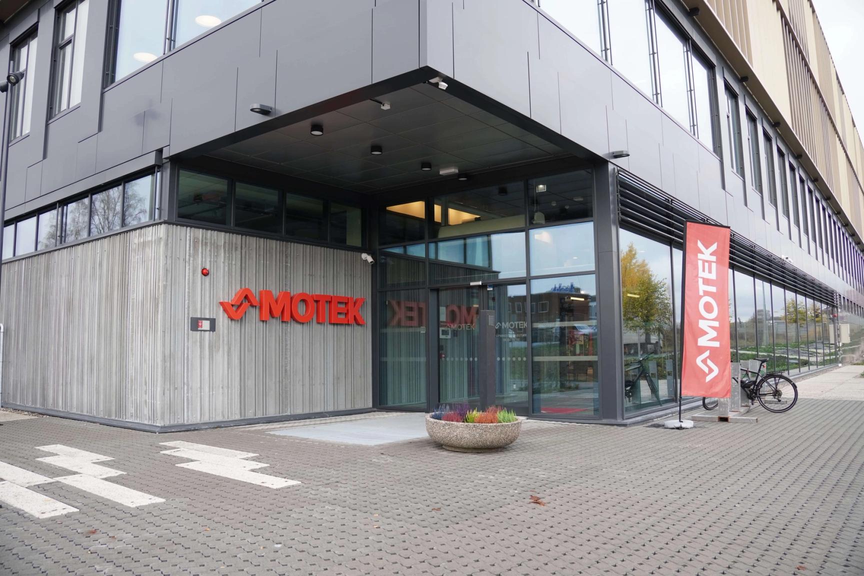 Exterior of the Motek office building with red logo signage on the facade and a branded banner beside the entrance.