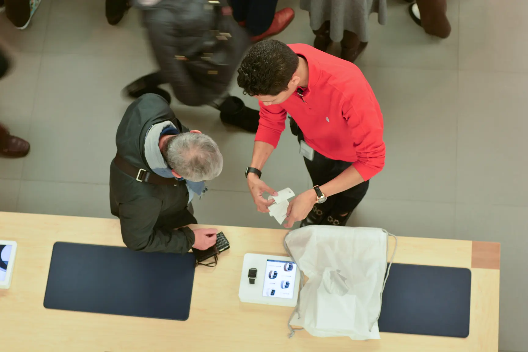 Overhead view of a retail store employee assisting a customer at a product display table in a busy store.