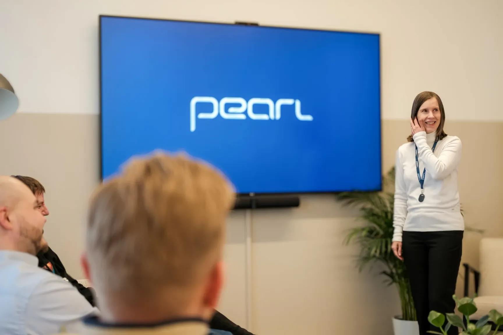 A woman presenting to a seated audience in front of a large screen displaying the Pearl Group logo in a meeting room.