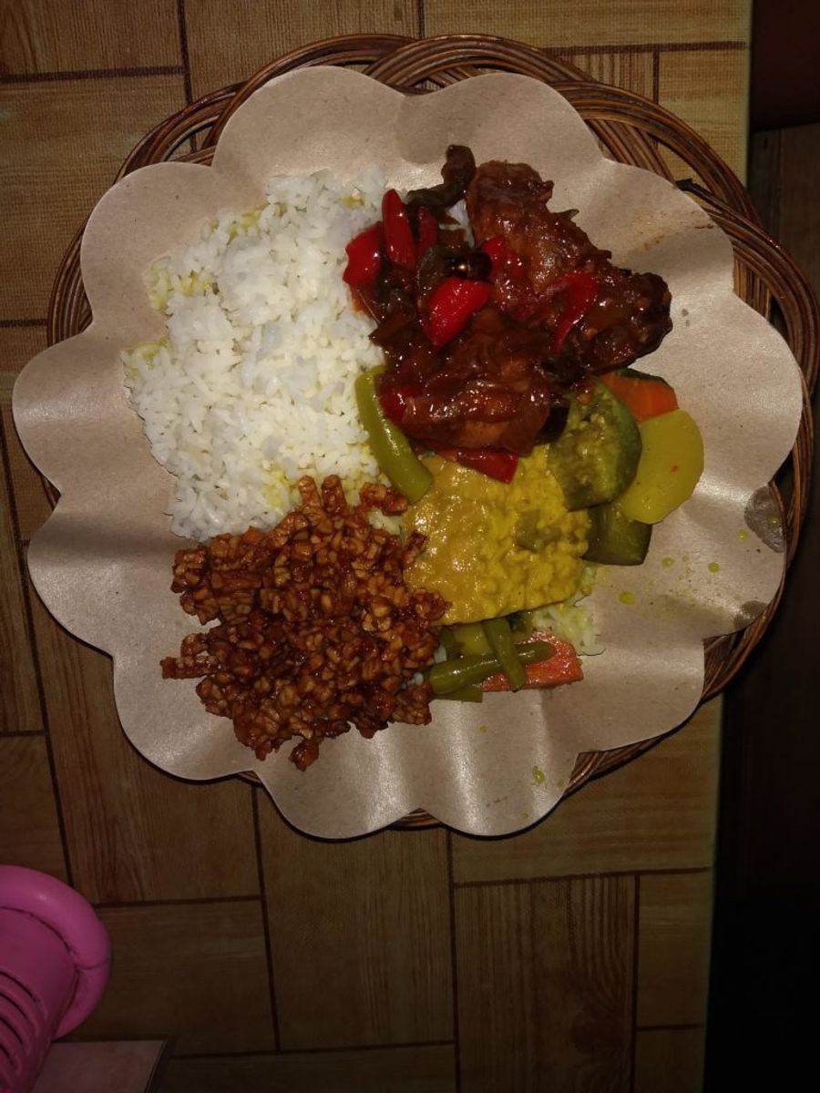 Nasi Campur - dole je tempe, vedle žluté tofu, zelenina a nahoře vařená rýže. Jídlo dostanete většinou v proutěném košíku s papírem.