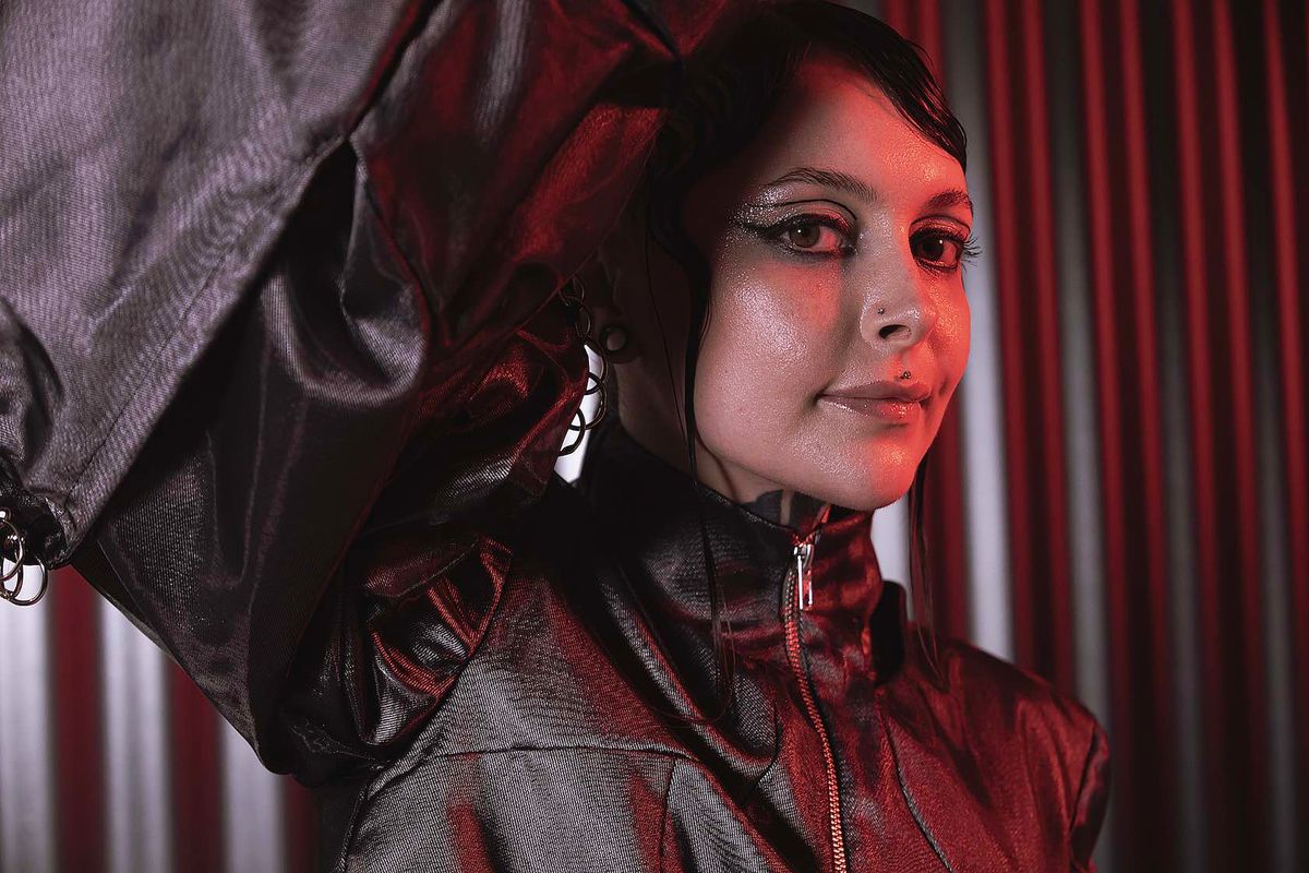 Close-up of Krista with an arm raised above her head, wearing a metallic jacket under red light
