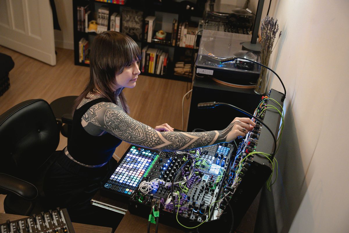 Krista seated in her studio, adjusting a densely patched modular synthesizer