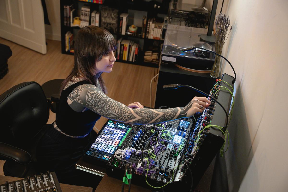 Krista seated in her studio, adjusting a densely patched modular synthesizer