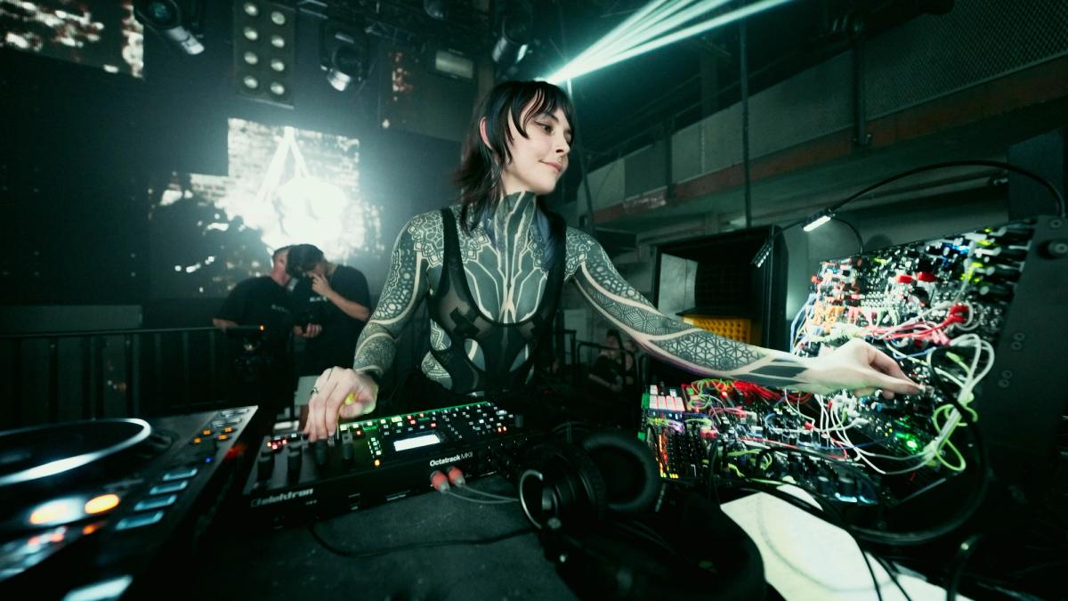 Krista performing with a modular synthesizer and DJ equipment beneath green stage lights