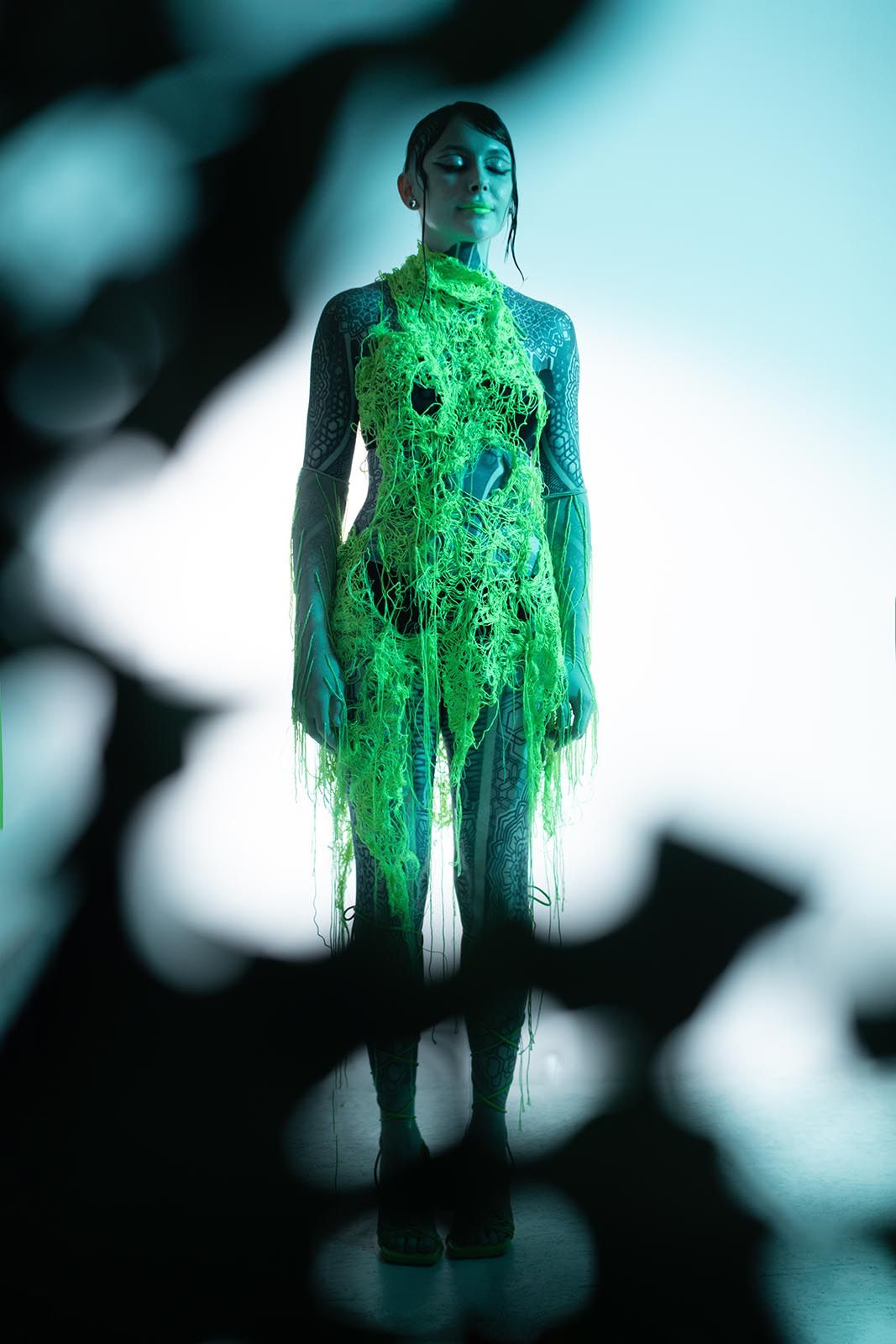 Krista wearing a bright green openwork dress under teal light and dramatic projected shadows
