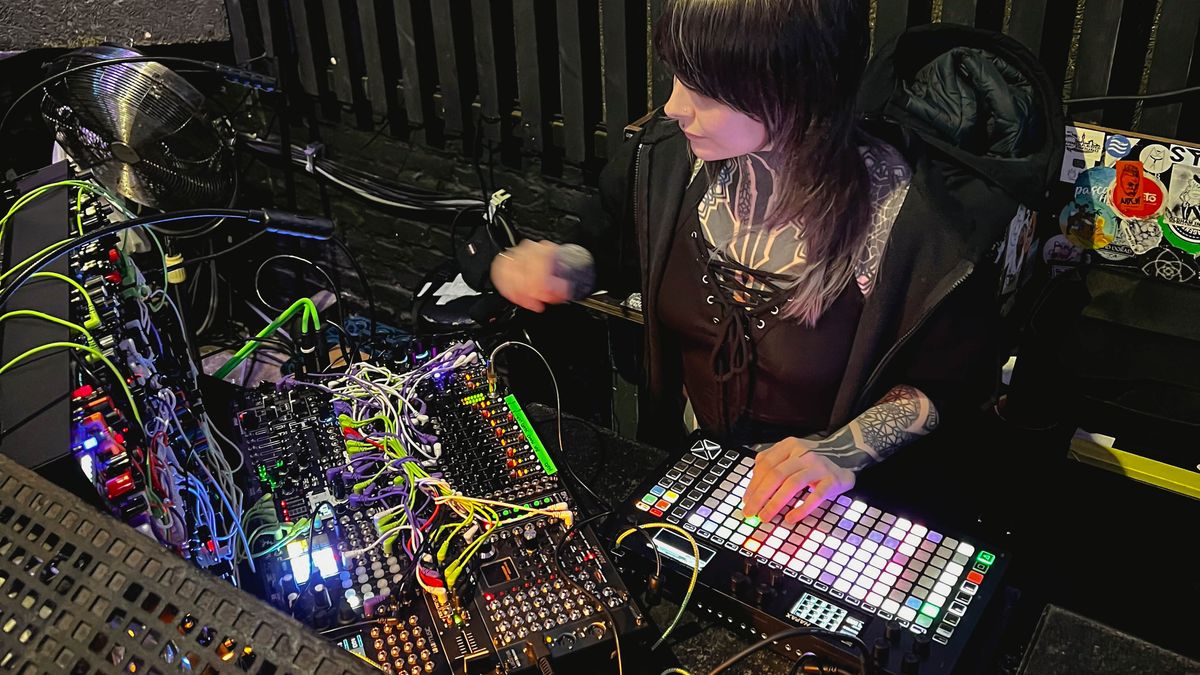 Krista operating an illuminated grid sequencer beside her modular synthesizer
