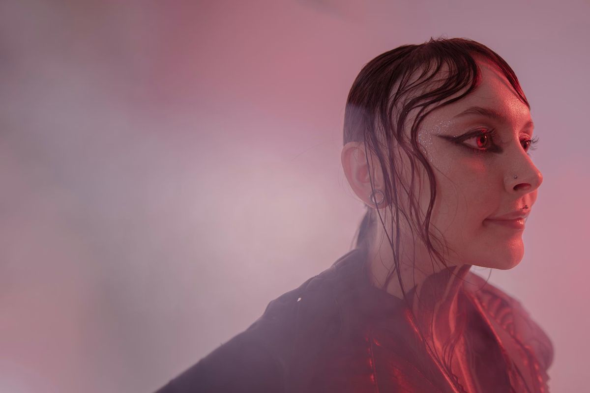 Krista in profile with a raised collar, lit by a soft red glow through studio haze