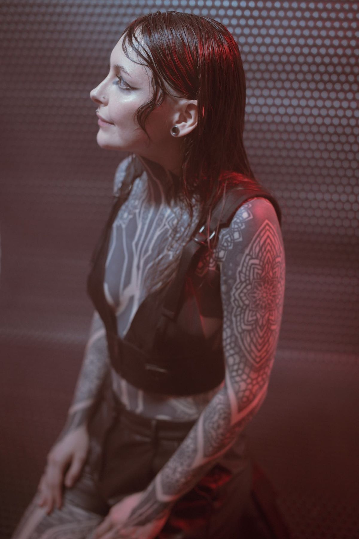 Krista Bourgeois in a black sleeveless top, looking left against a textured metal backdrop