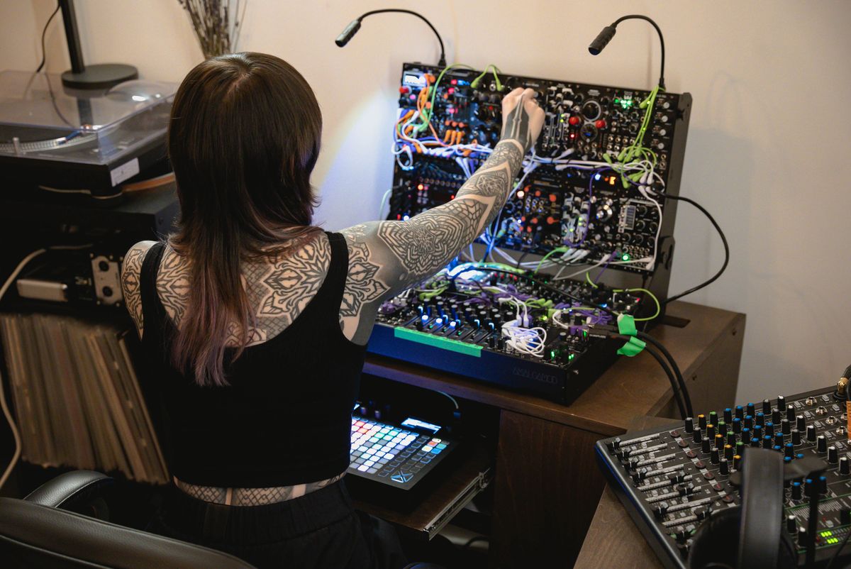 Krista seen from behind reaching to adjust the top row of her studio modular synthesizer