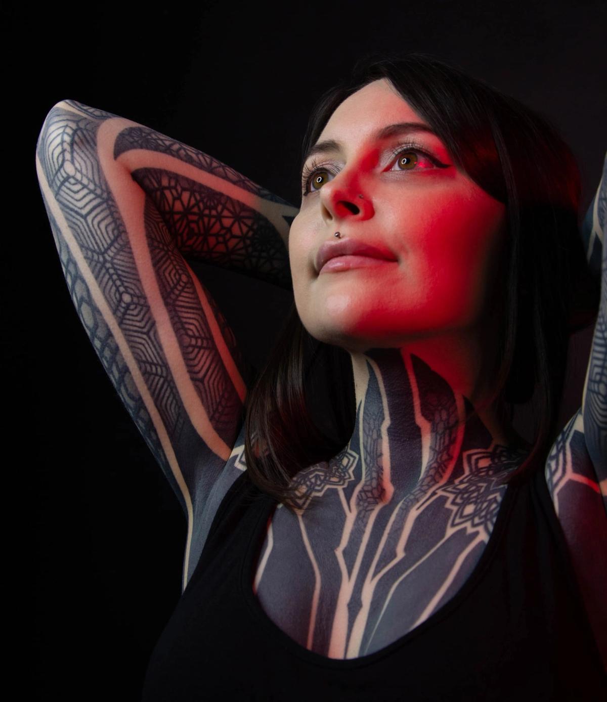 Portrait of Krista looking upward with her arms raised, lit in red against a black background
