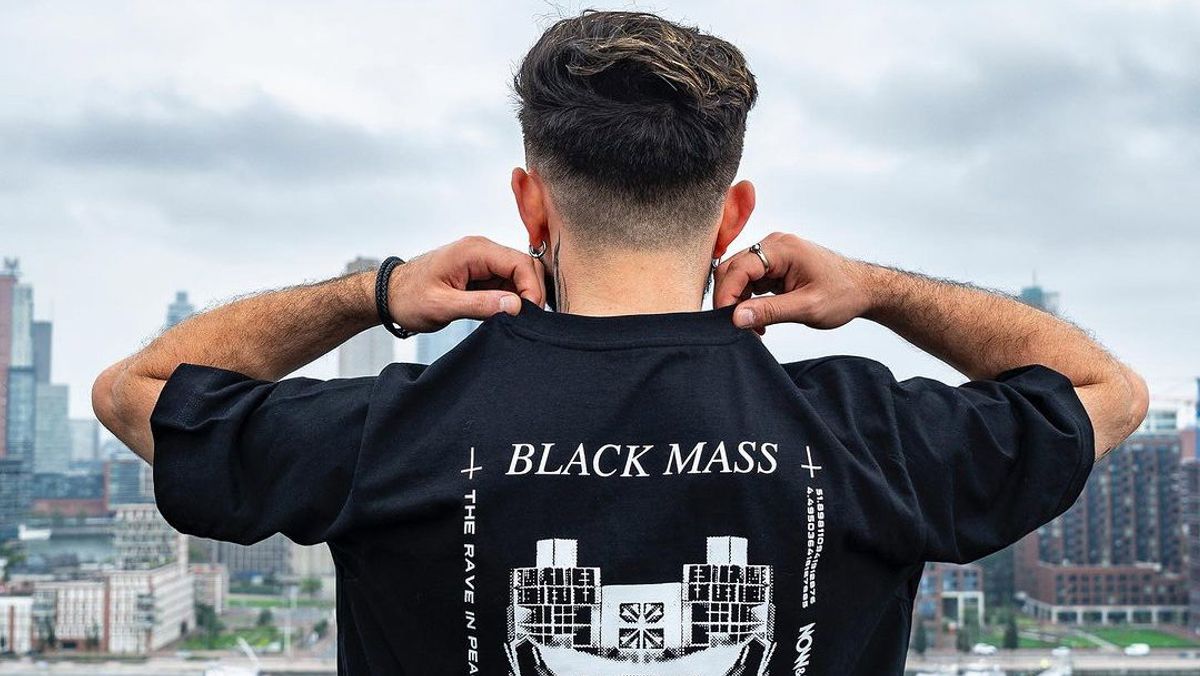 A person seen from behind adjusting a black Black Mass T-shirt on a rooftop above the city