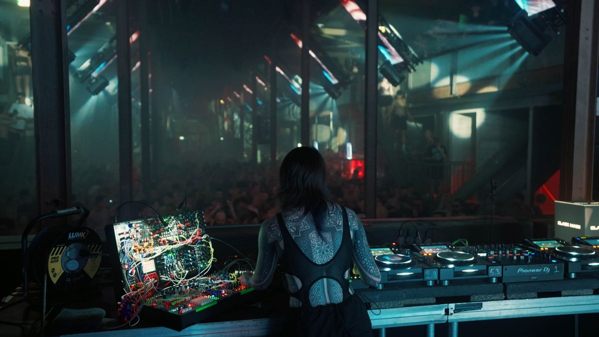 Rear view of Krista performing at a booth with her modular case and DJ decks facing a dark venue
