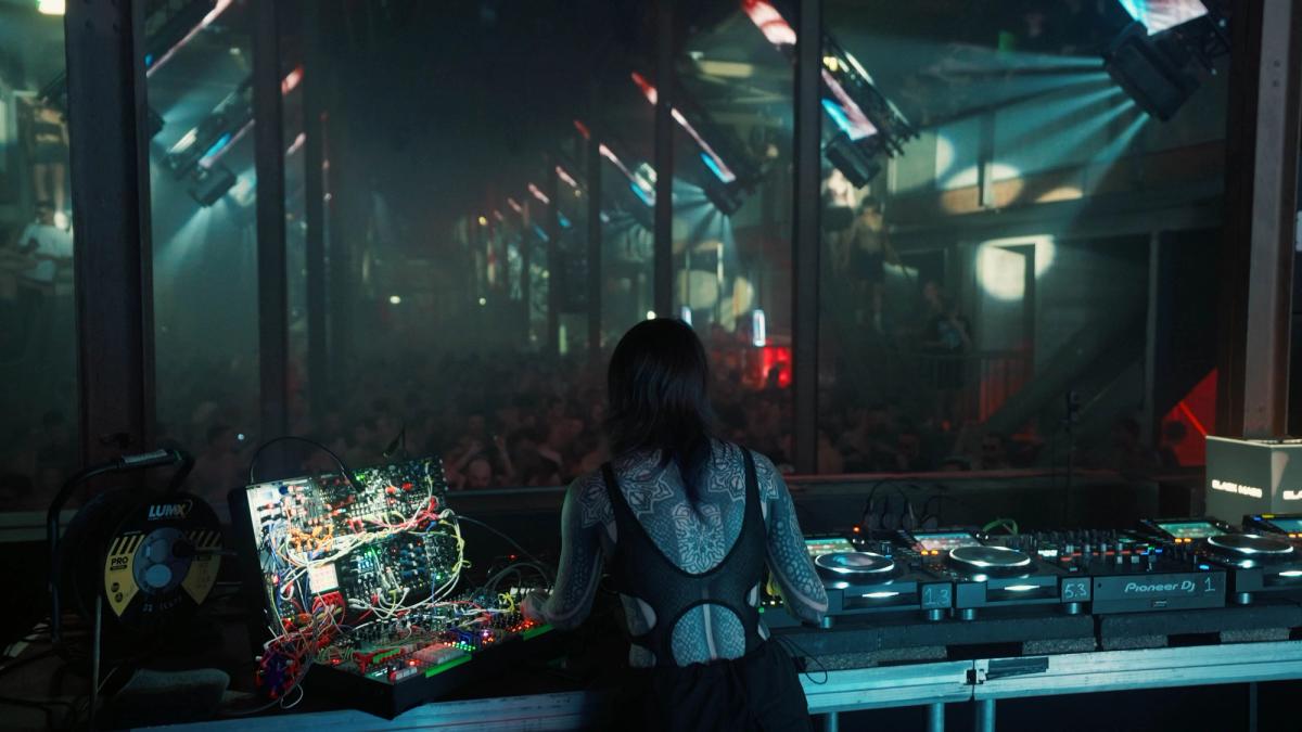Rear view of Krista performing at a booth with her modular case and DJ decks facing a dark venue