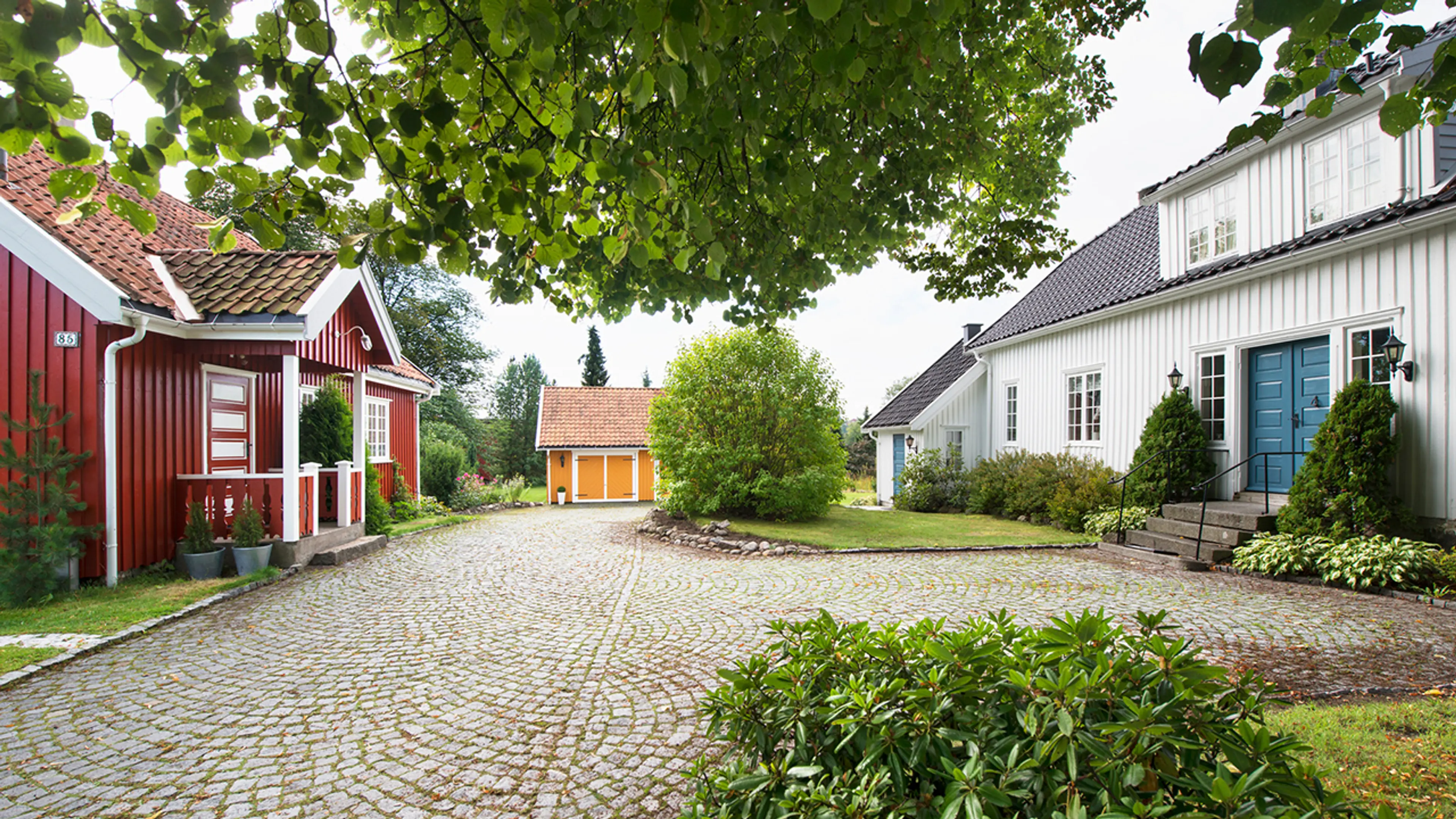 Gårdstun med brostein og hus malt i hvitt, gult og rødt.