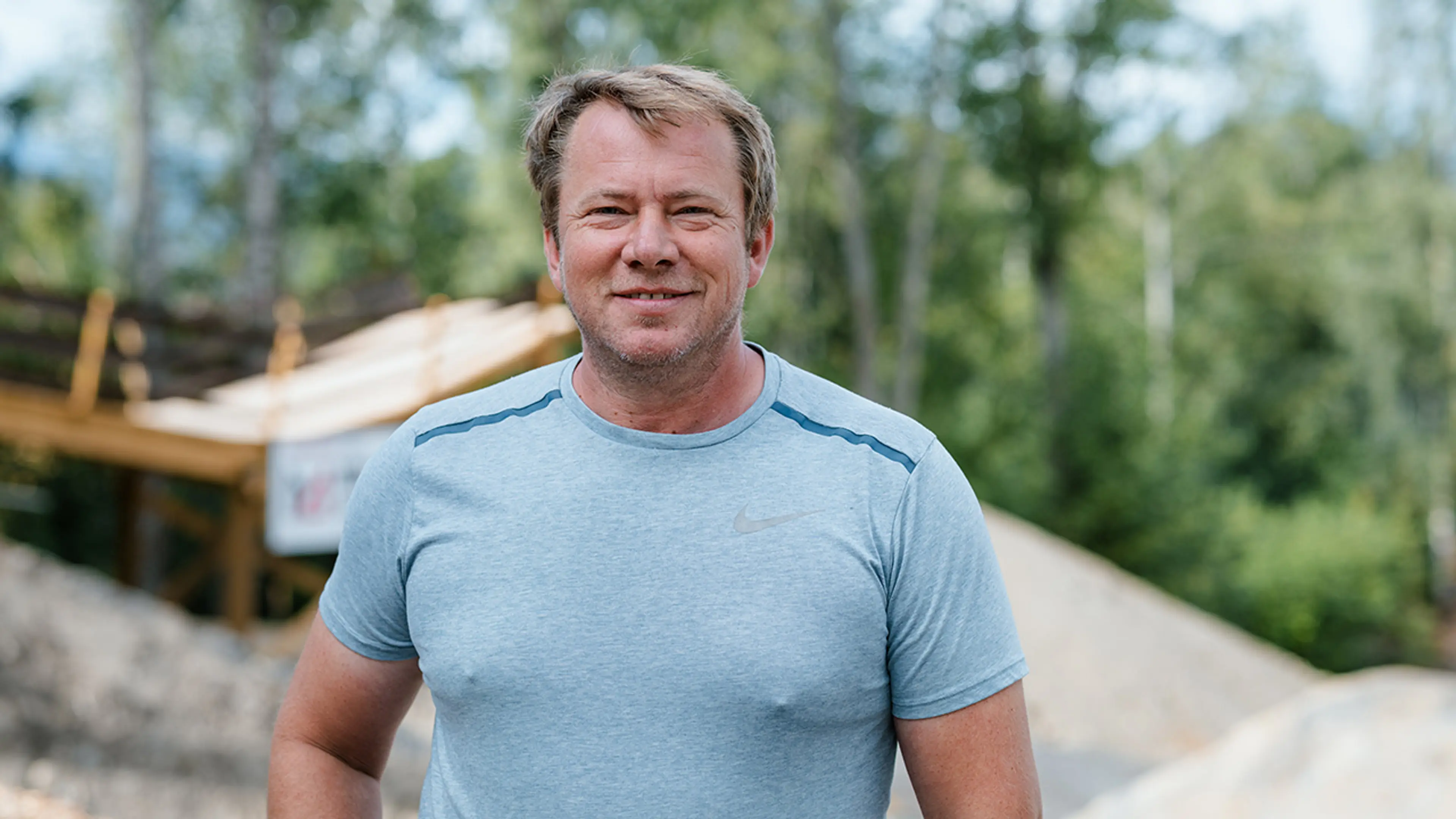 Mann med lys blå t-skjorte som står ute på en sykkepark og smiler til kameraet.