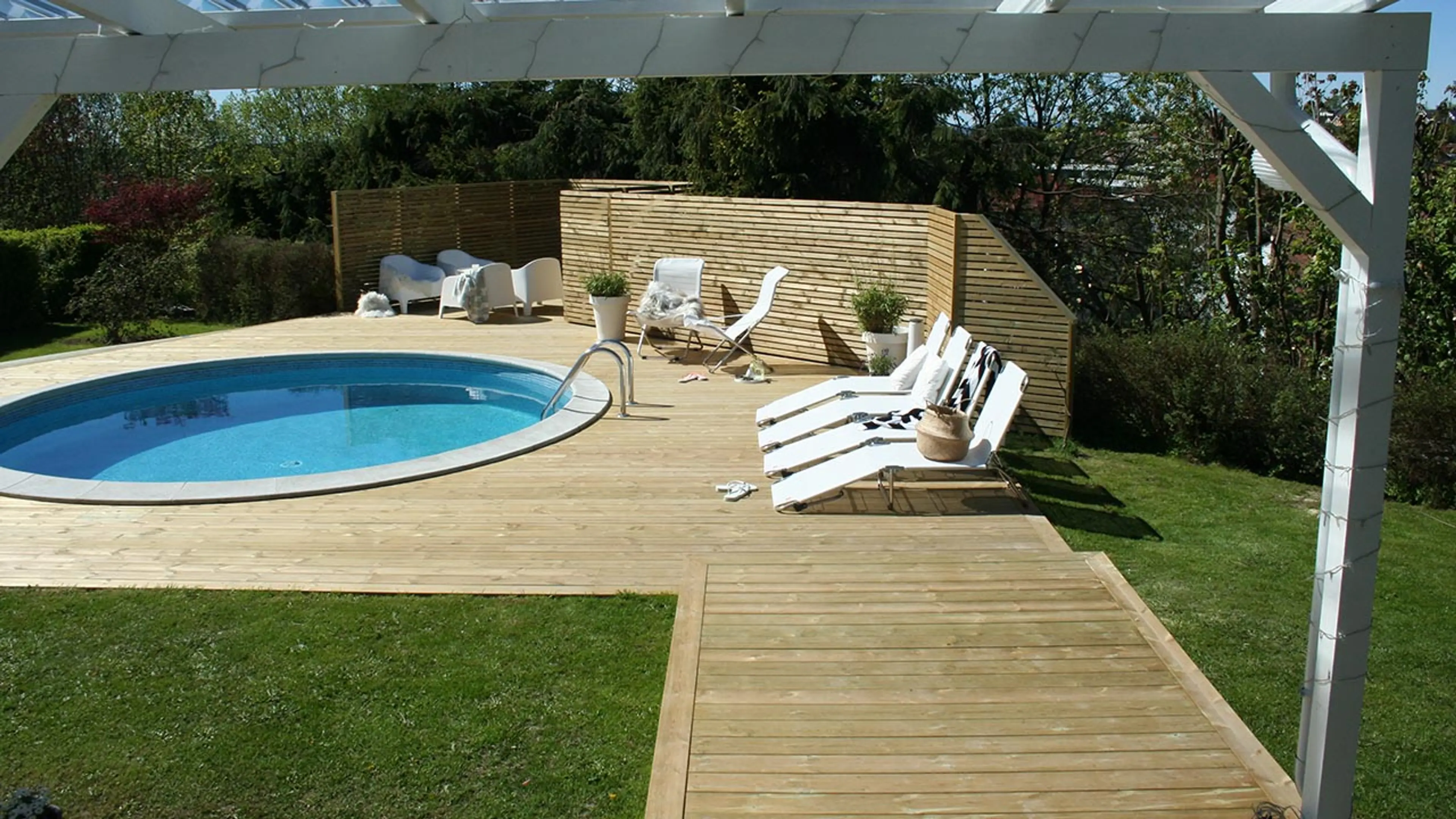 Trykkimpregnert terrasse med svømmebasseng, solstoler og levegg.