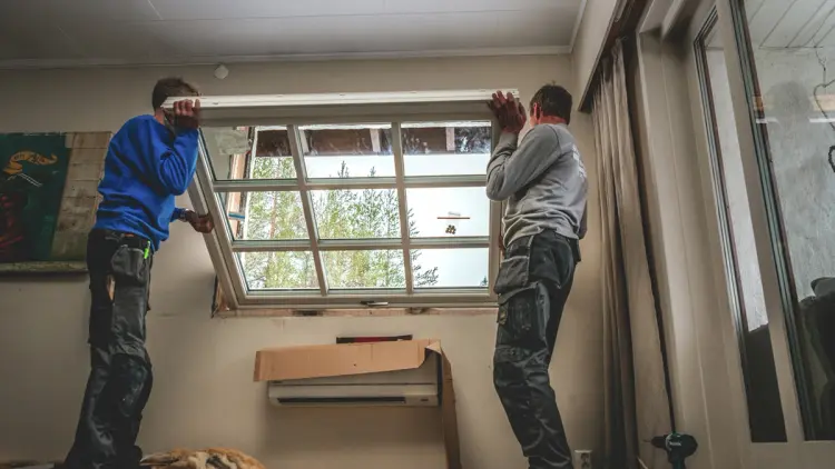To menn som holder på å bytte vinduer.