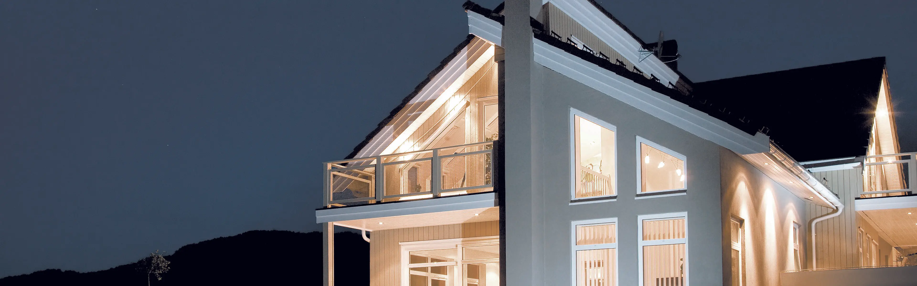 Hvitt, moderne hus med store pvc-vinduer sett utenfra om kvelden.