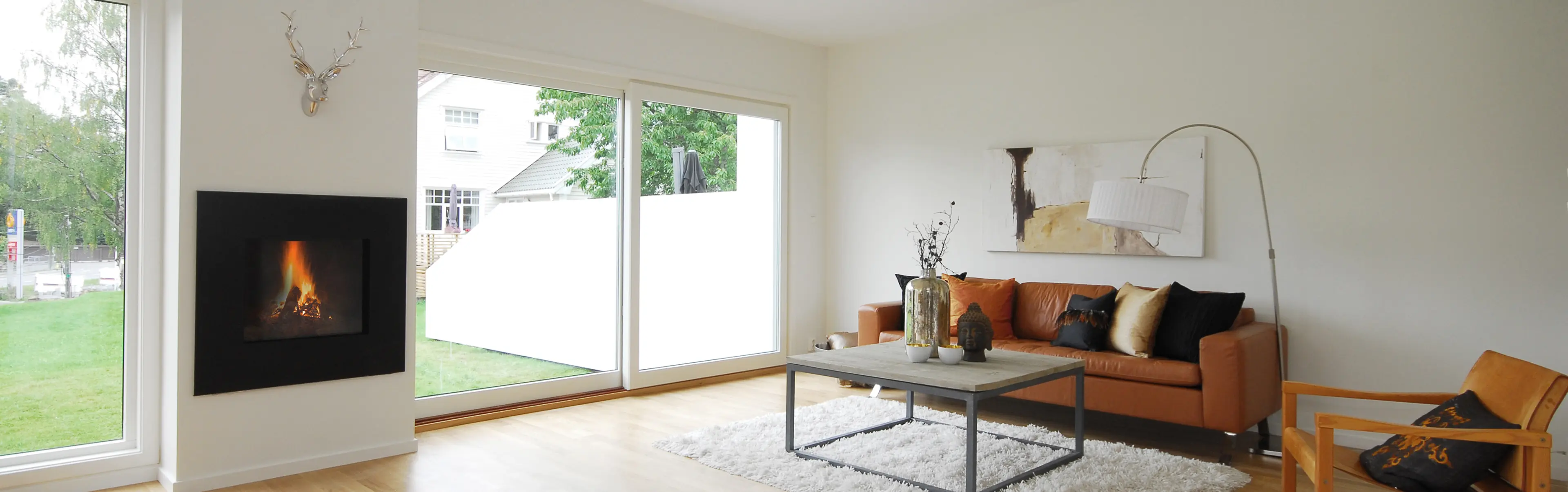 moderne stue med store vinduer mot hagen. Brun skinnsofa og peis i veggen.