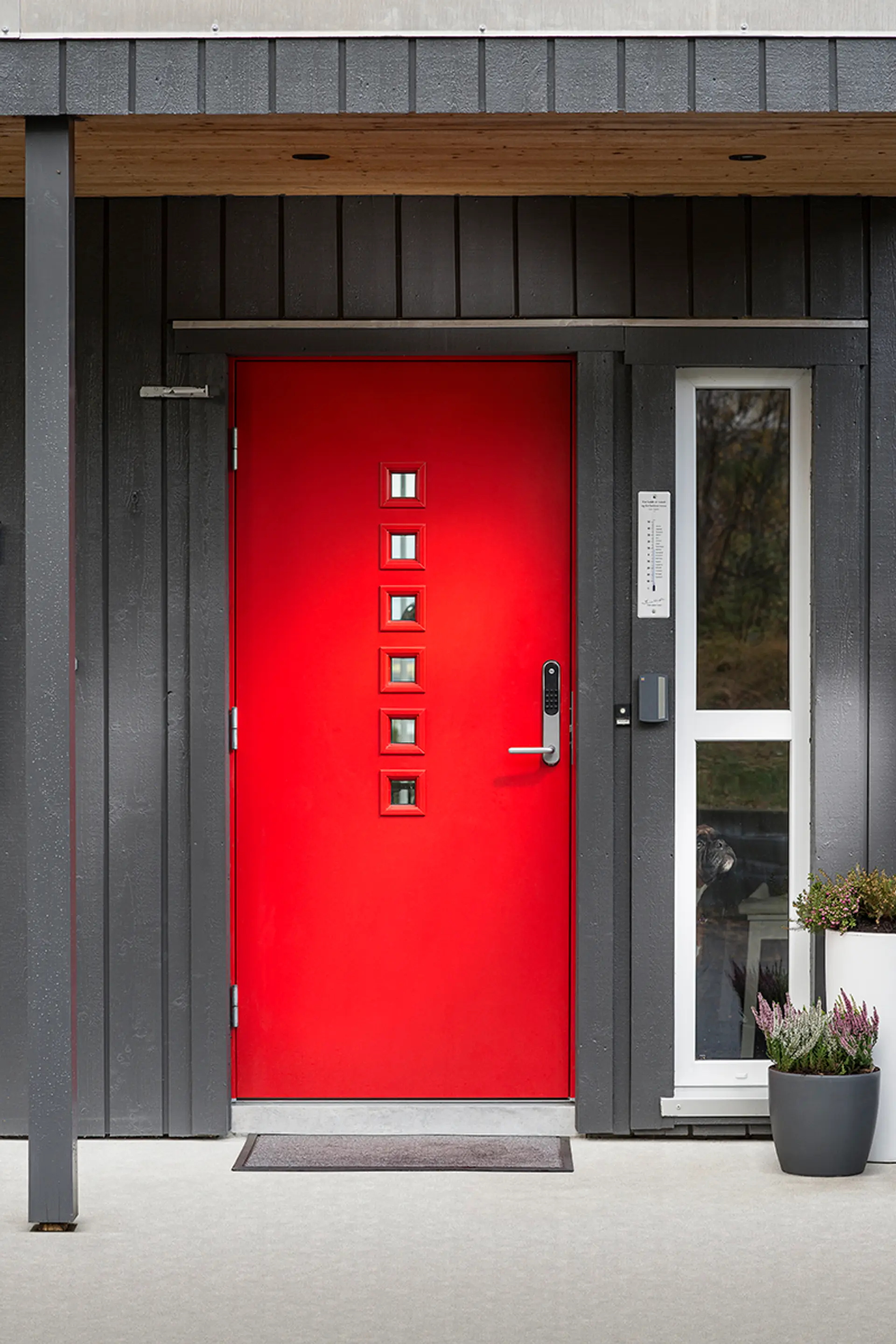 Rød ytterdør på grått hus.