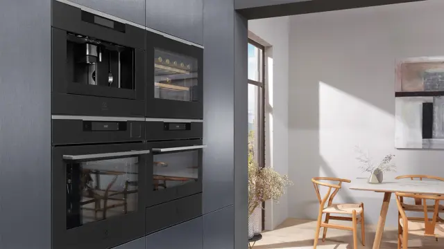 Sorte hvitevarer i høyskap på mørkt kjøkken.