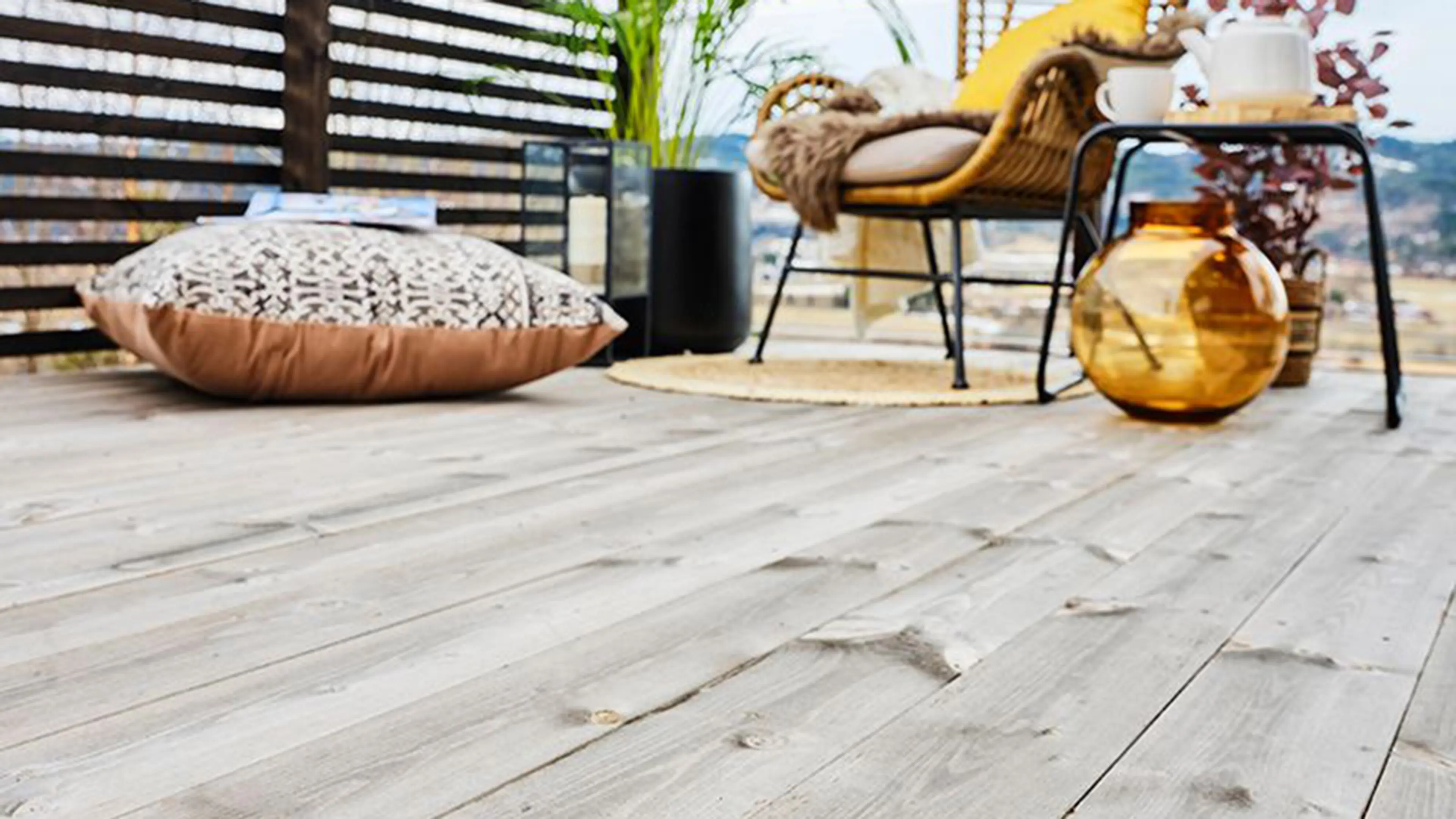 Koselig uteplass med kurvstol, teppe og grønn plante i hjørnet av en terrasse