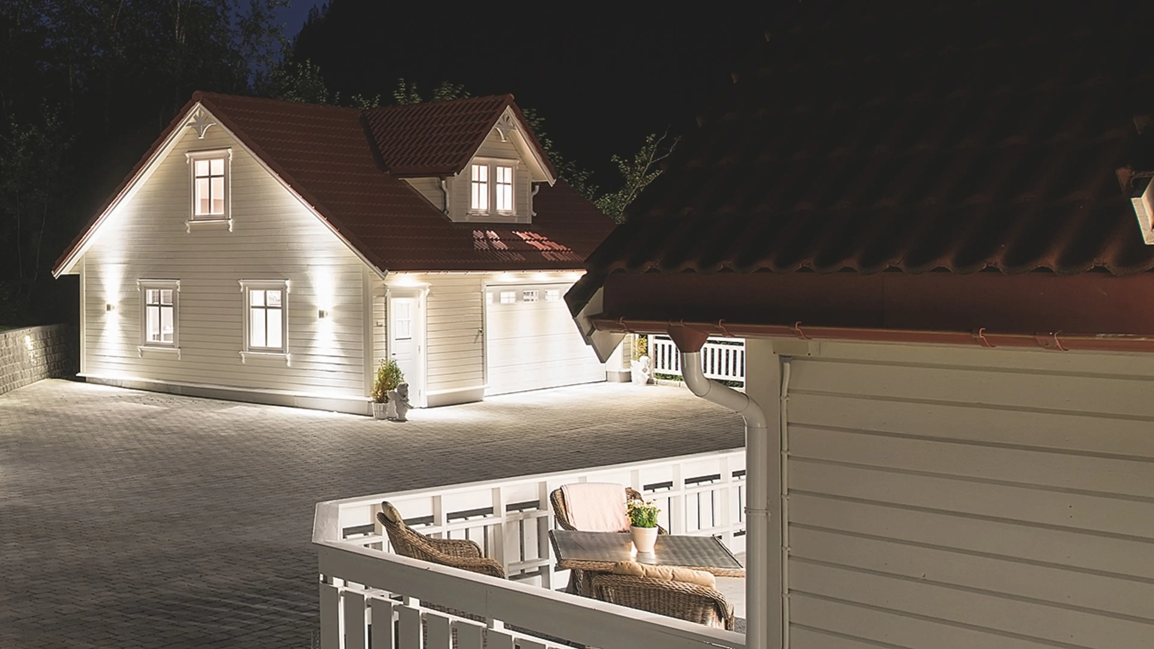 Hvitt hus med garasje som er opplyst med utebelysning til garasje.