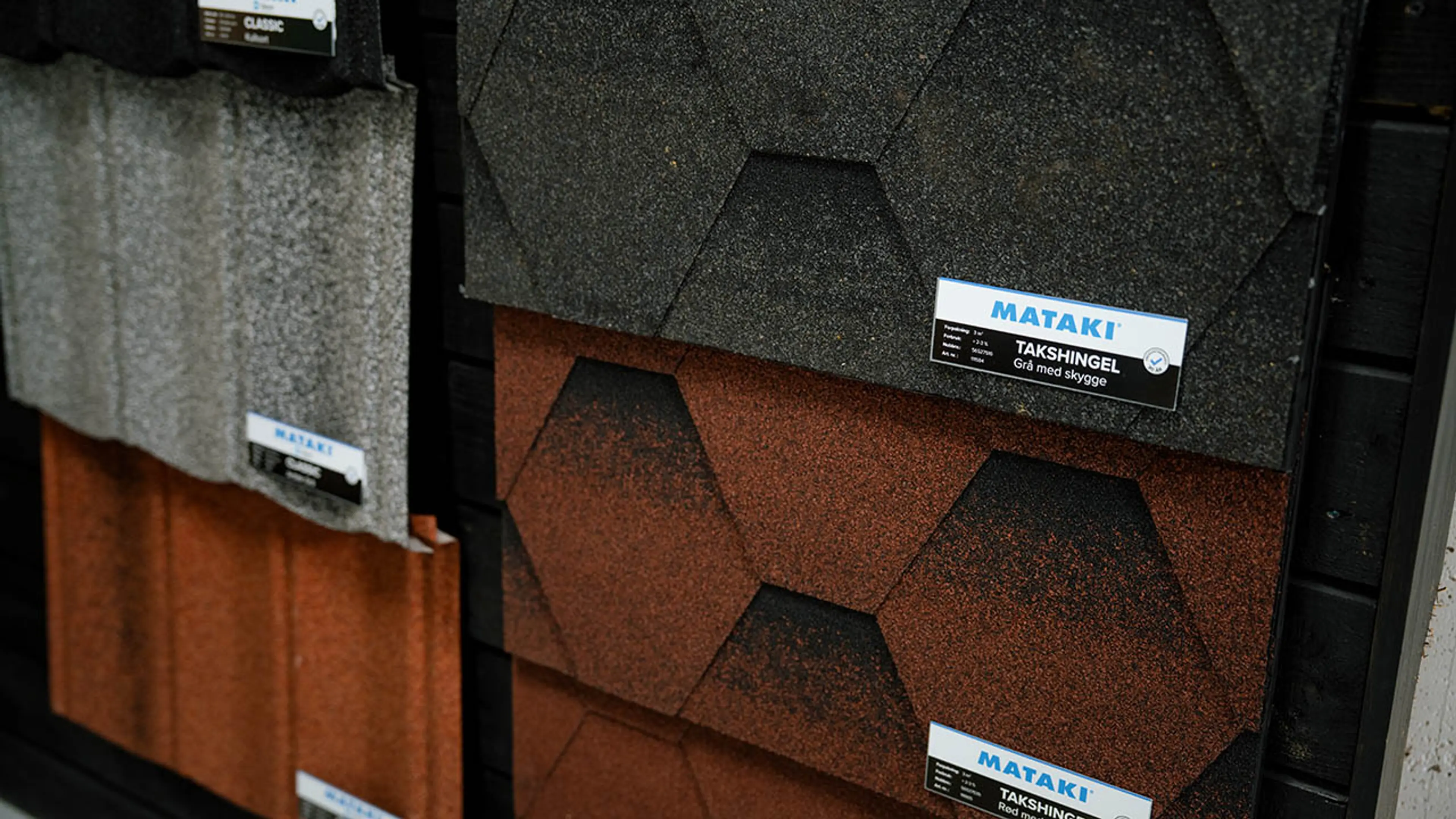 Rød og svart takshingel på vegg i byggevarehus.