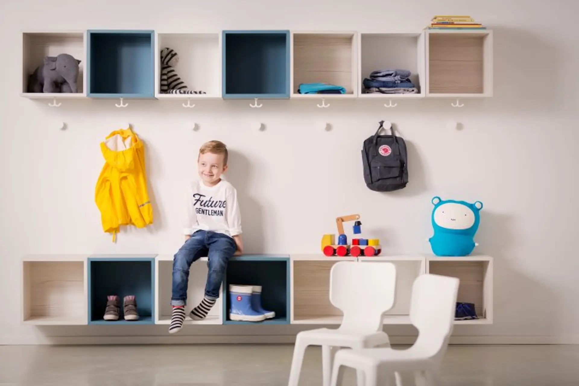 ung gutt sitter i garderoben i barnehage. Gipsplater på veggene.