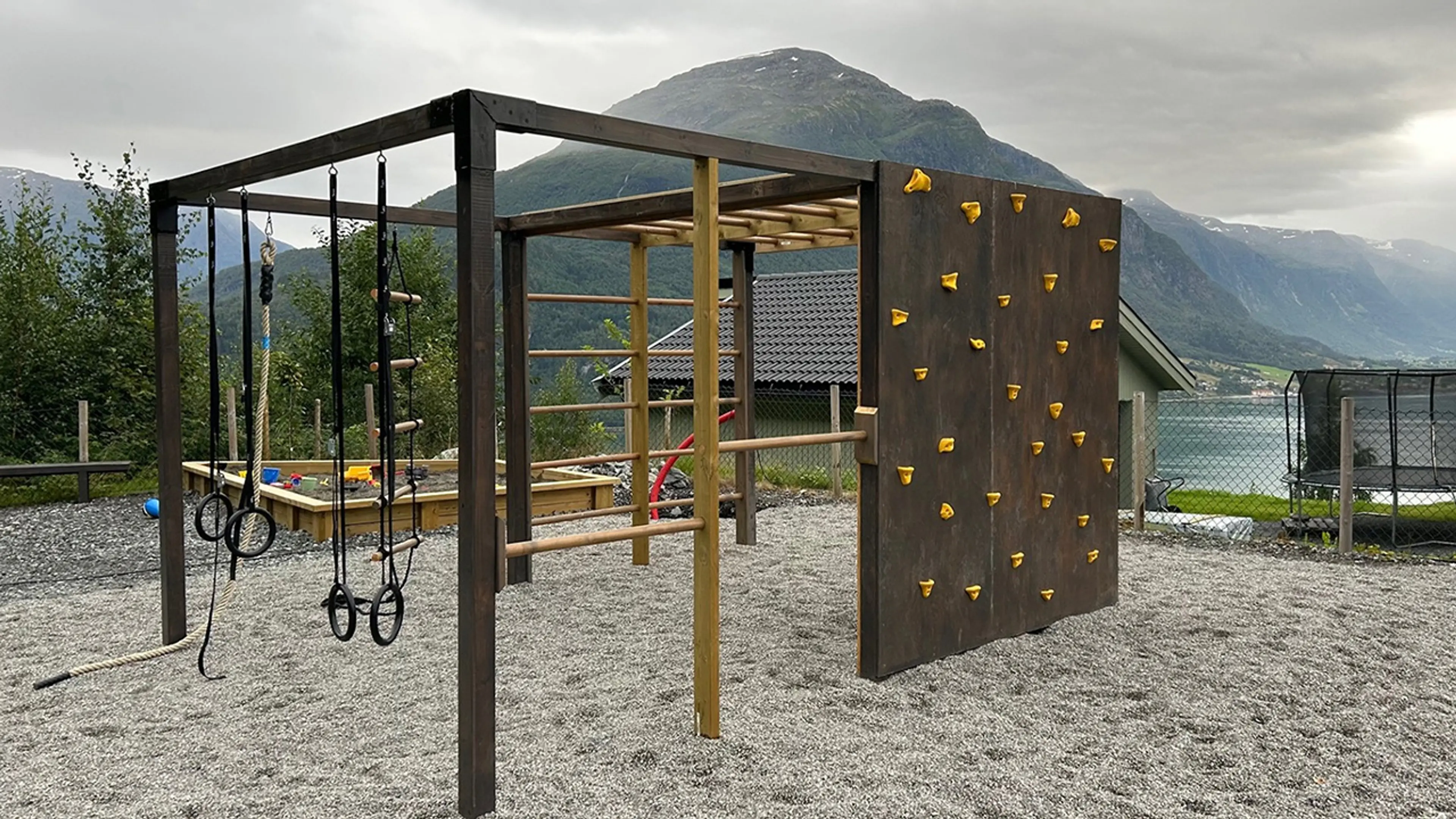 Stort klatrestativ med klartevegg og ringer på en lekeplass ved havet.
