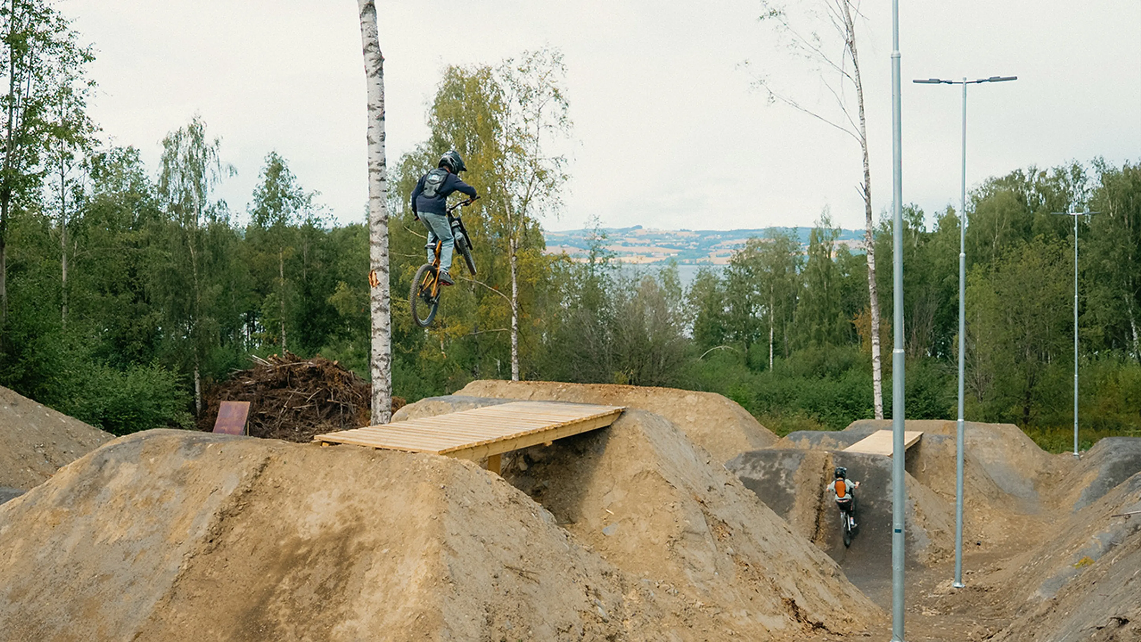 2 ungdommer som hopper på sykkel i en sykkelpark i skogen.