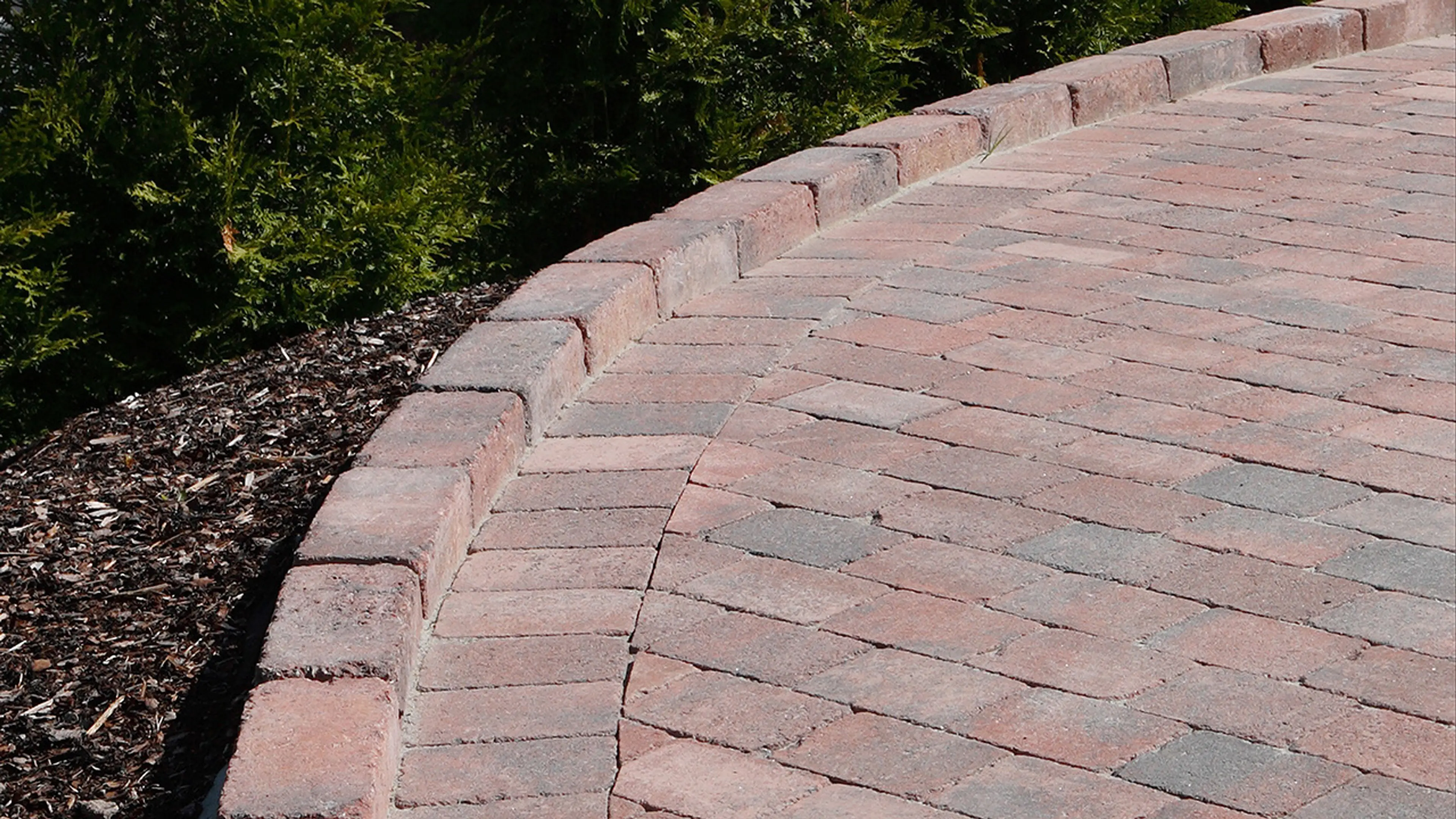 Gårdsplass med belegningsstein i rødmix lagt i bue.