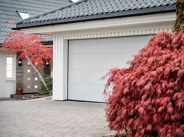 hvitmalt garasje og garasjeport med flotte, rosa busker på utsiden