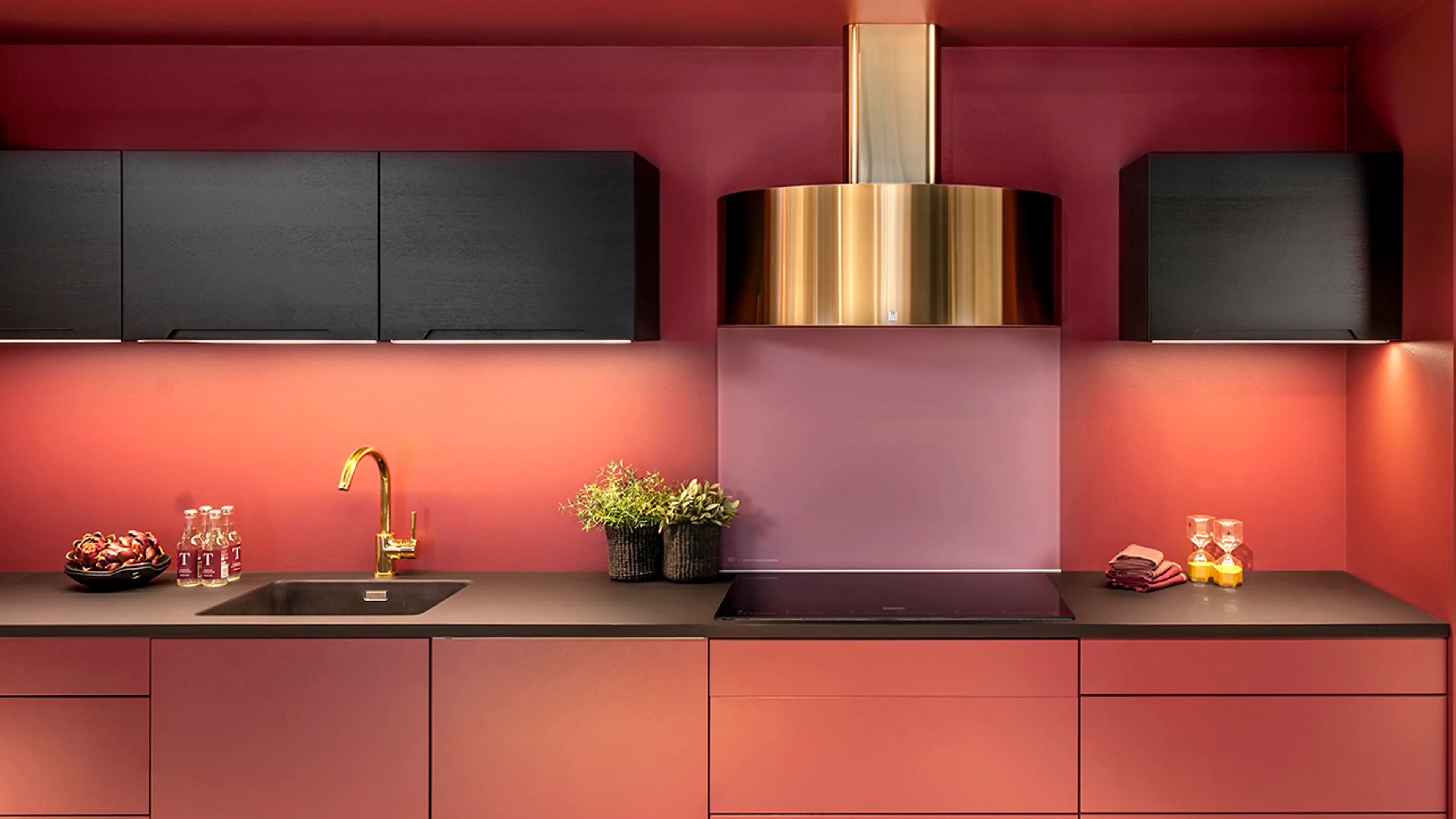Kjøkkenhette i kobber fra RørosHetta på rødt kjøkken med sorte og rosa detaljer.
